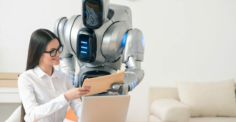 This one for you.  Content charming positive smiling girl sitting at the table and working on the laptop while getting package from the robot